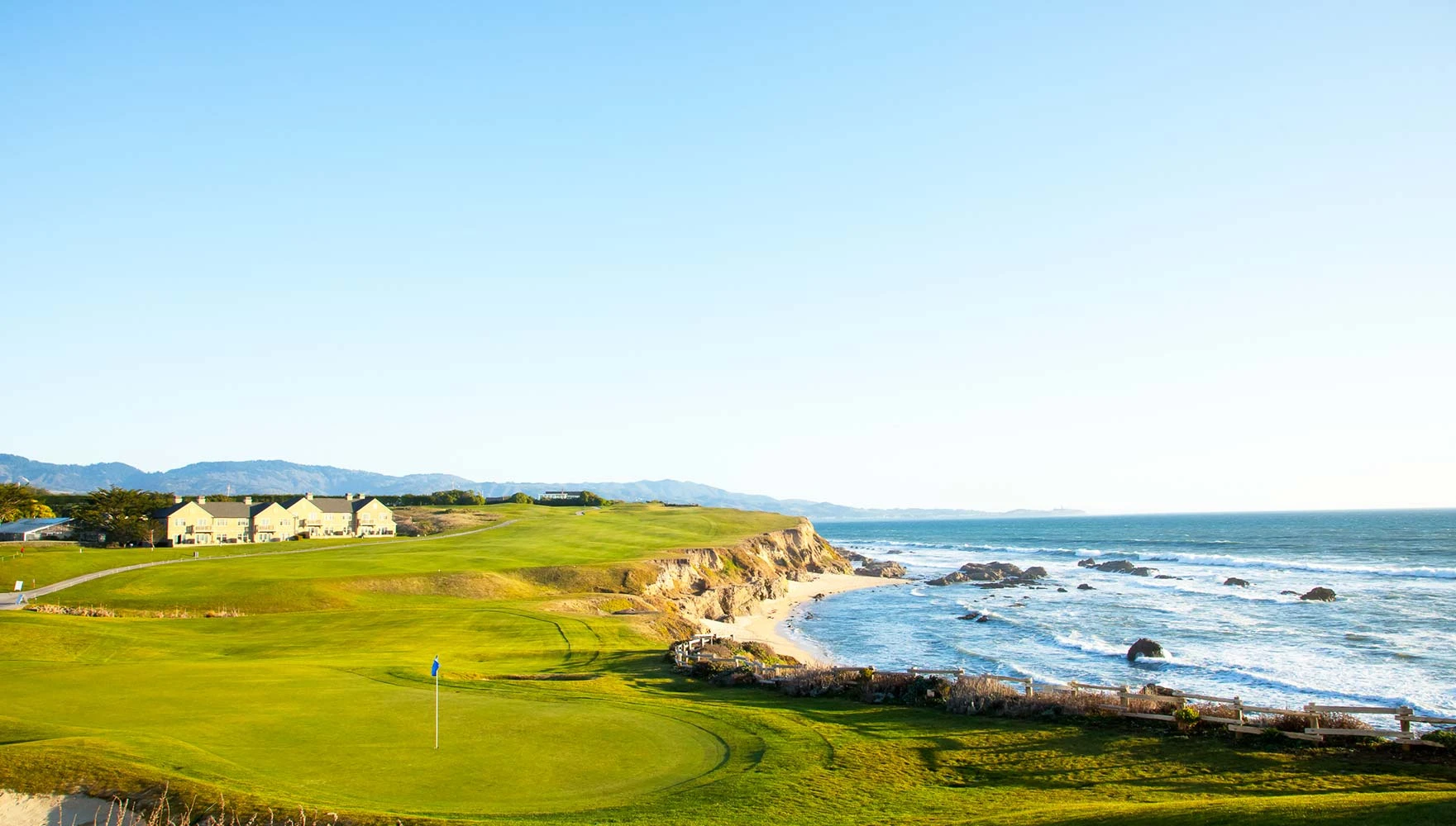 Scenic golf course beside a rocky coastline under clear blue sky.